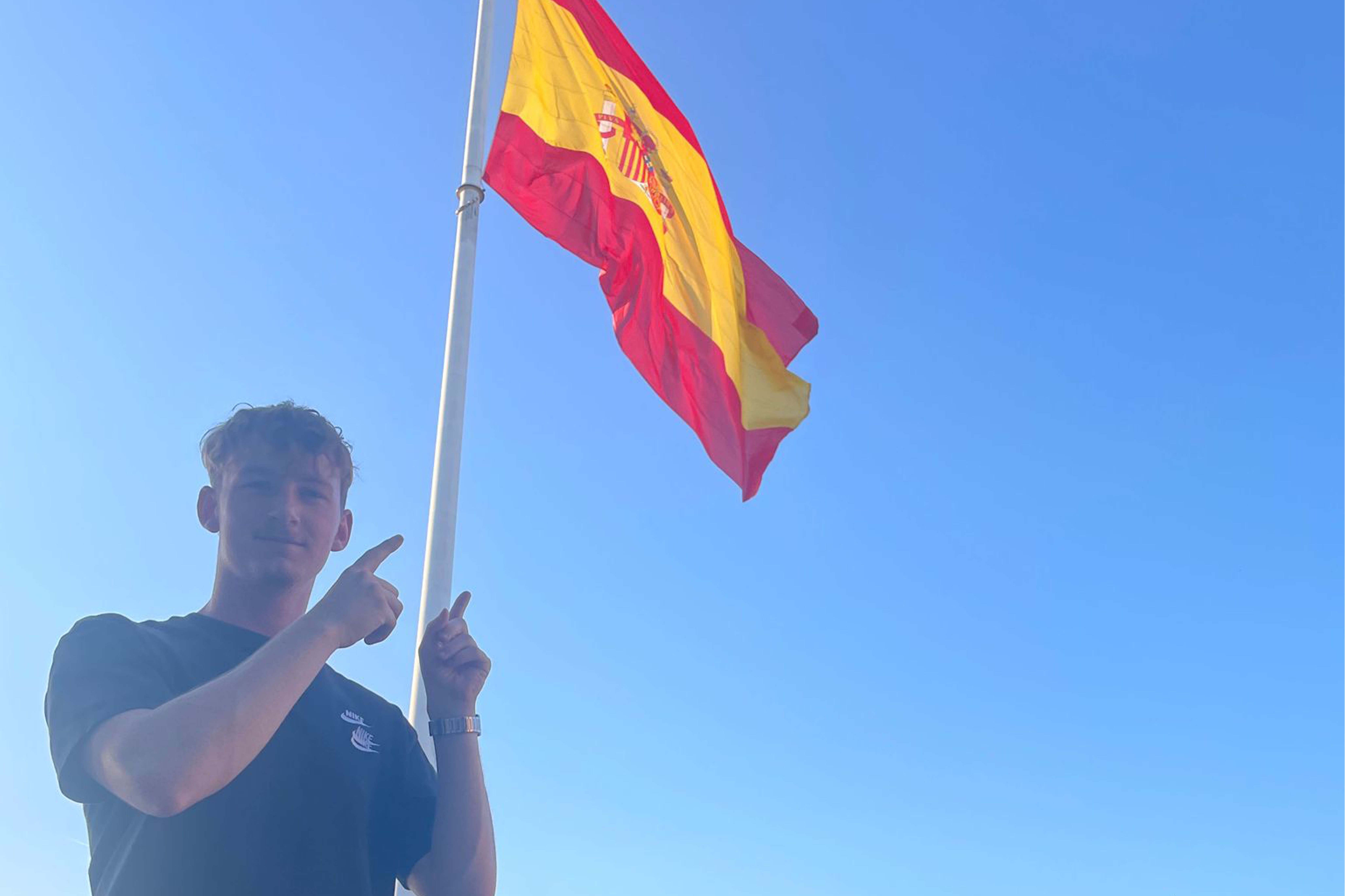 Een jonge man tegen de achtergrond van de blauwe lucht en de Spaanse vlag.