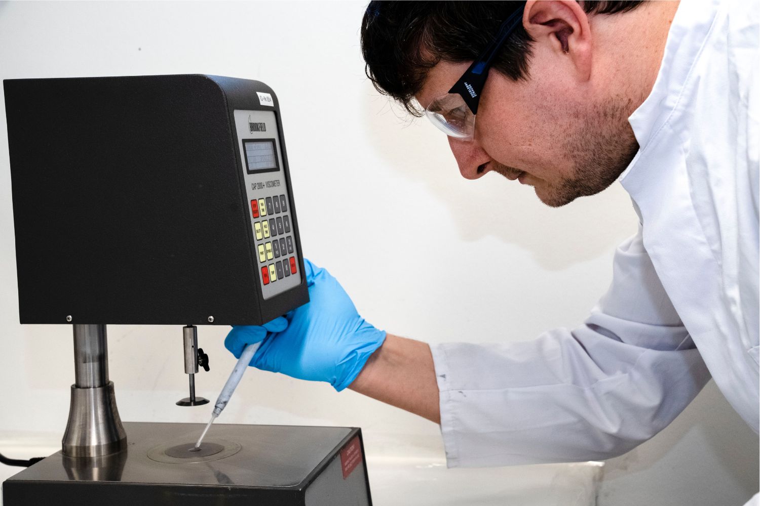 Un homme en blouse blanche verse quelque chose à l'aide d'une pipette sur une surface